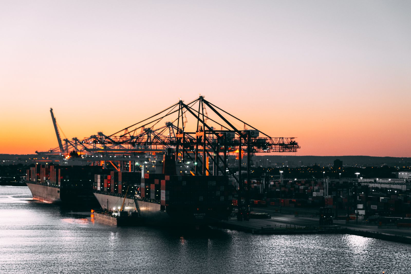 Container ship and gantry cranes at a working port at dusk